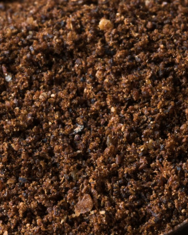 A close-up view of ground cloves spices in a bowl, showing their coarse and crumbled texture.